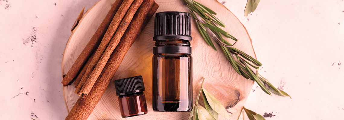 Essential oils with cinnamon sticks and green leaves on a wooden surface.