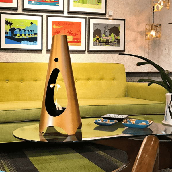 Modern gold indoor ethanol fireplace on a coffee table in a living room with green sofa and framed art