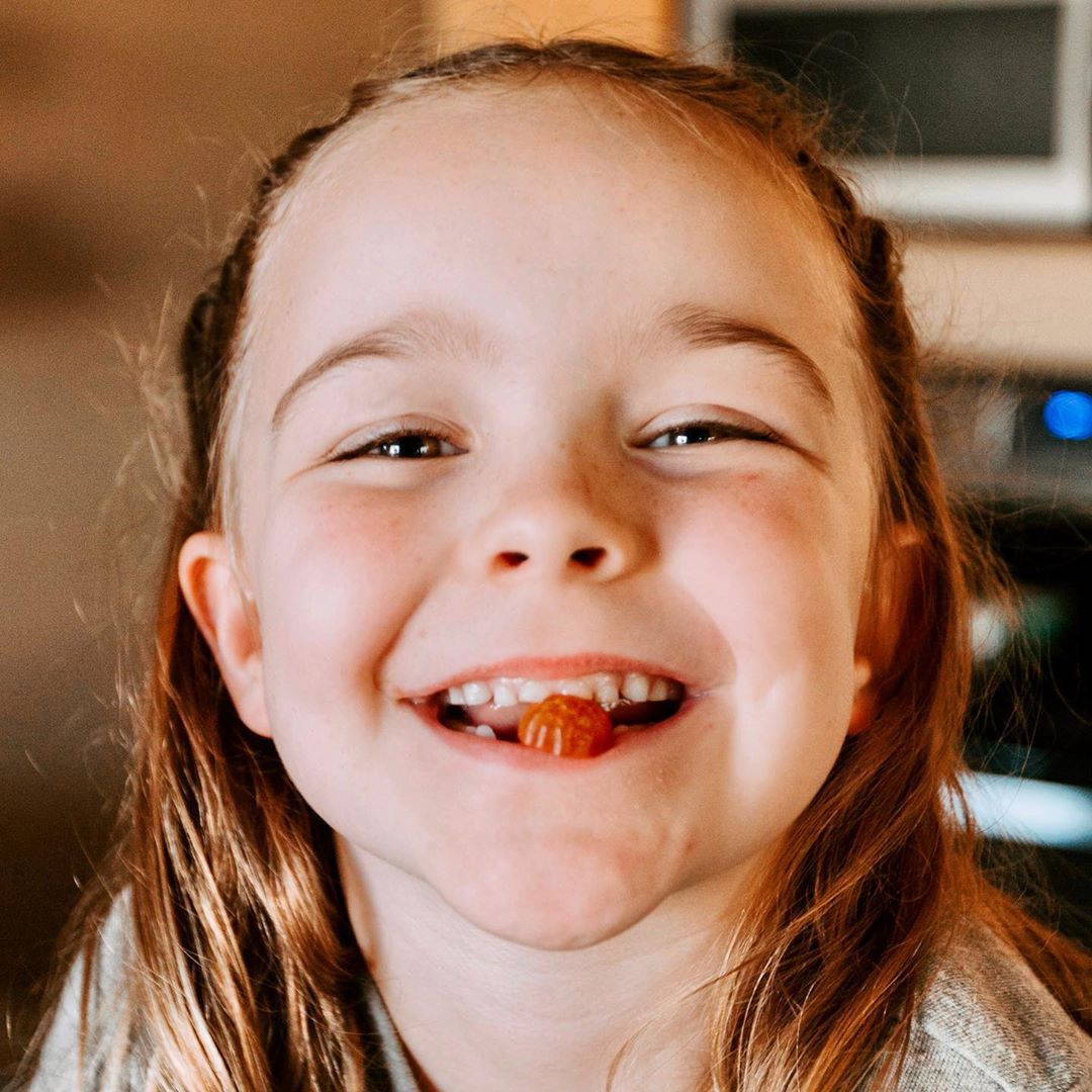 A young girl smiling with a First Day gummy in her mouth