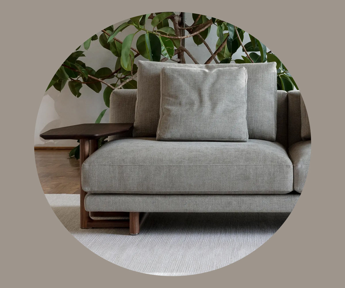 A modern Abacus grey sofa with a cushion and side table, surrounded by greenery.
