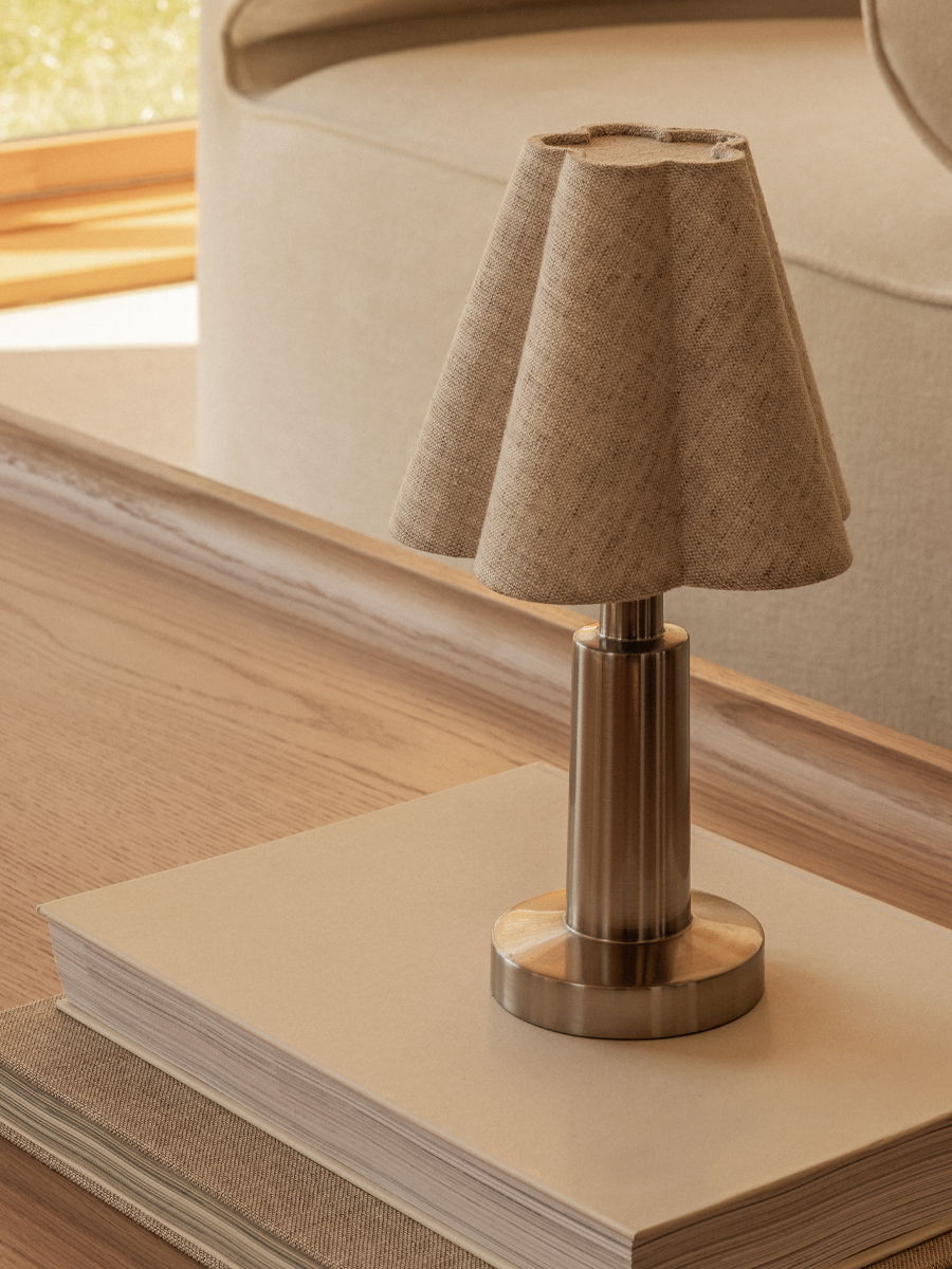 A small Admiral by Audo lamp with a fabric shade on a table.