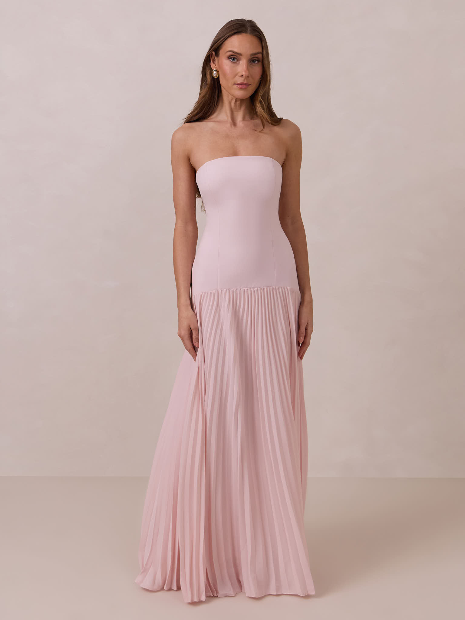 Woman in a strapless pink gown standing against a neutral background.