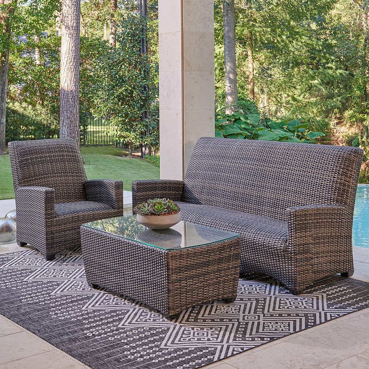 Outdoor seating area with a sofa, chair, and coffee table on a rug.