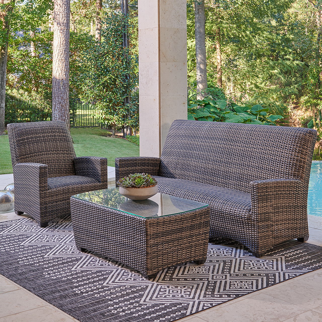Outdoor seating area with a sofa, chair, and coffee table on a rug.
