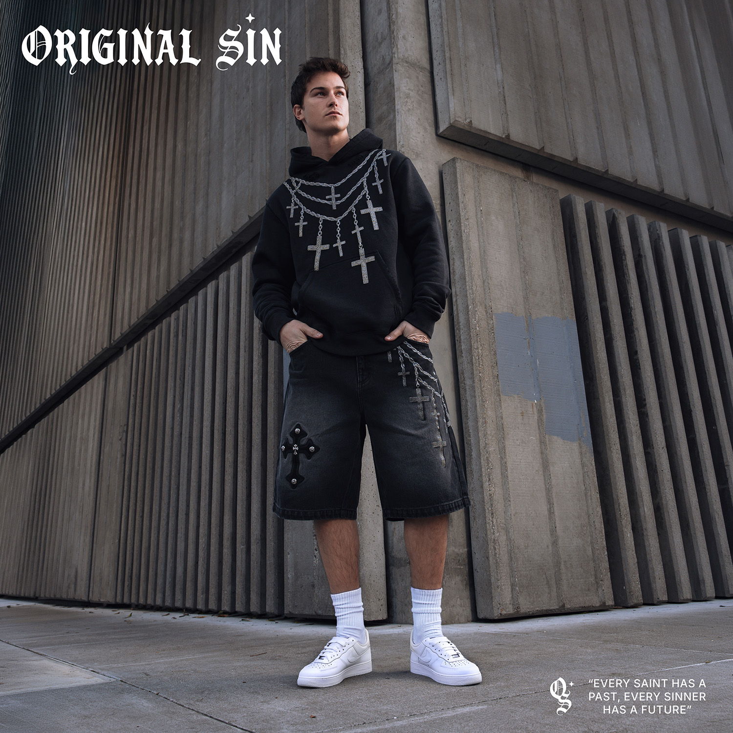 Person in a black hoodie and shorts standing against a textured wall.