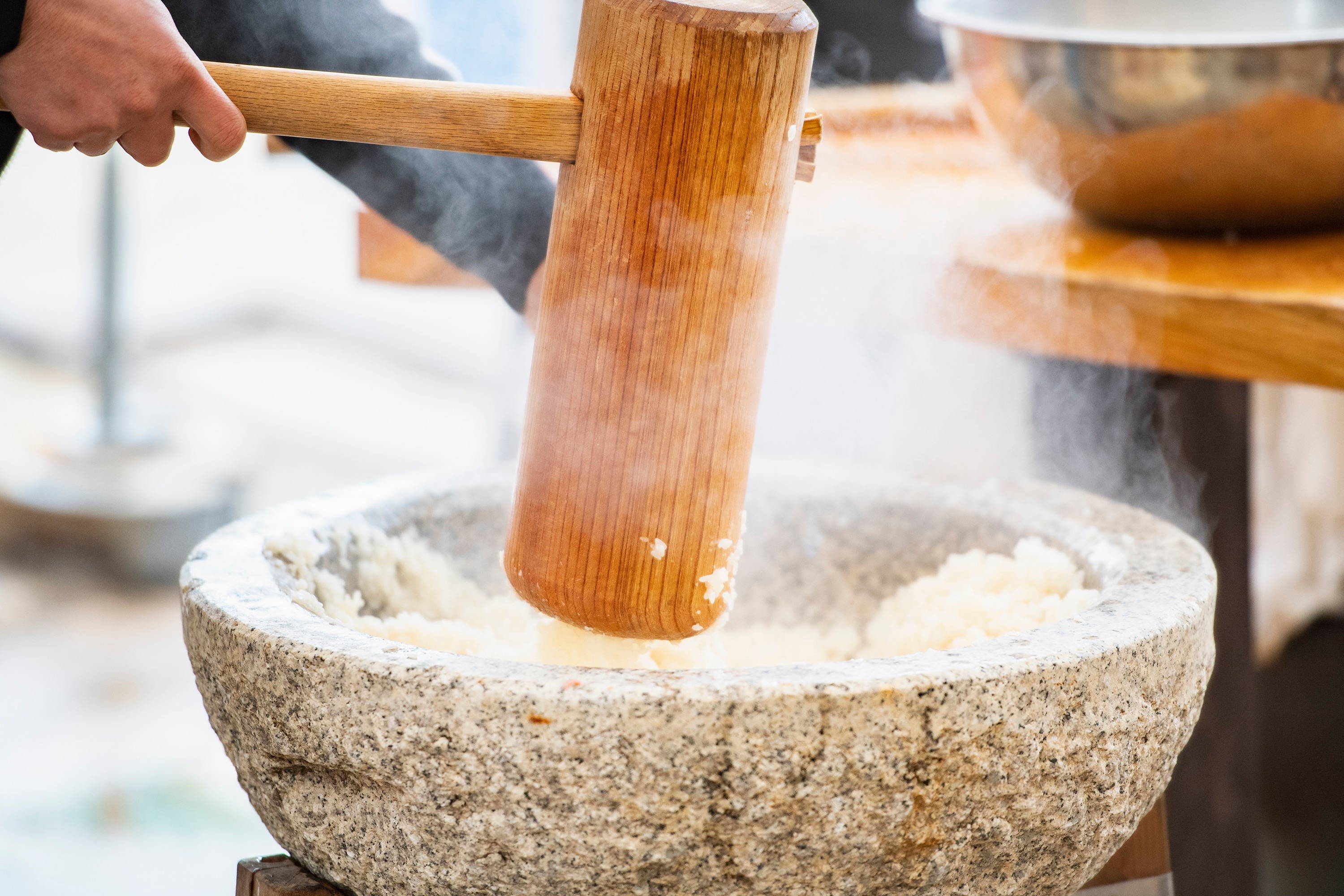 pounding steamed rice grains using mortar and pestle.