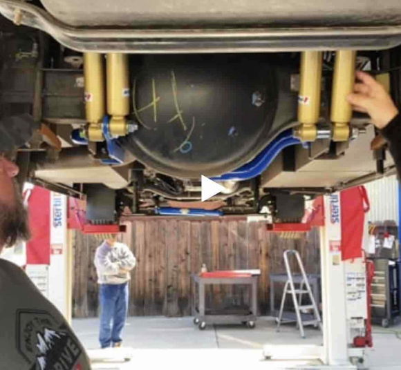 Two people working on a vehicle's underside in a garage.