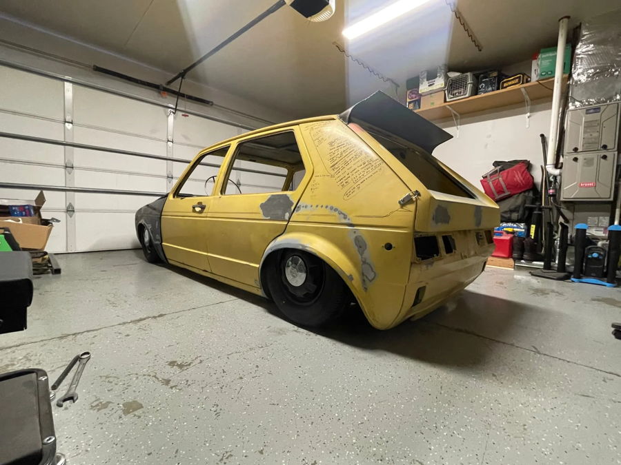 Rear three-quarter view of yellow 1982 Volkswagen Rabbit Slam in garage hatch open custom bodywork featured customer install gallery photo 1