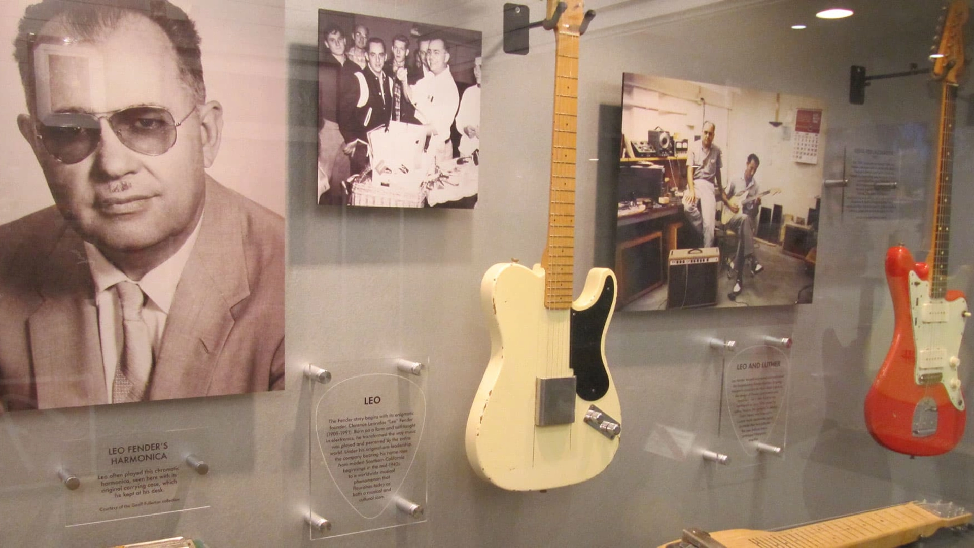 Guitars displayed alongside historical photographs of Leo Fender in a museum setting.