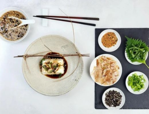 Plated dish with tofu, garnishes, and side ingredients on a table.