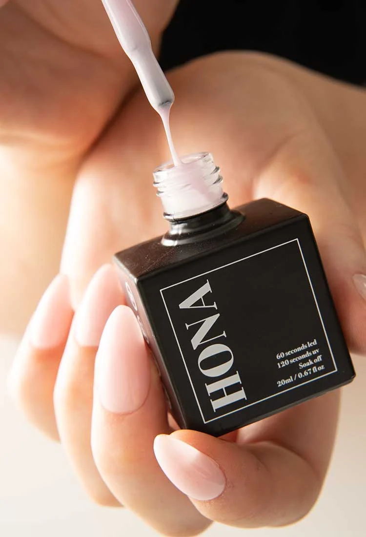 A hand holding a black nail polish bottle with a brush above it.
