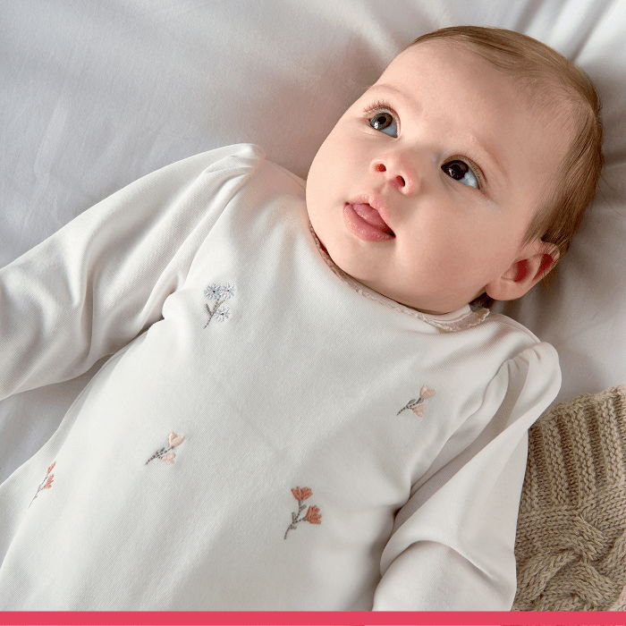 Baby lying on a soft surface, wearing a light-colored outfit with floral designs.
