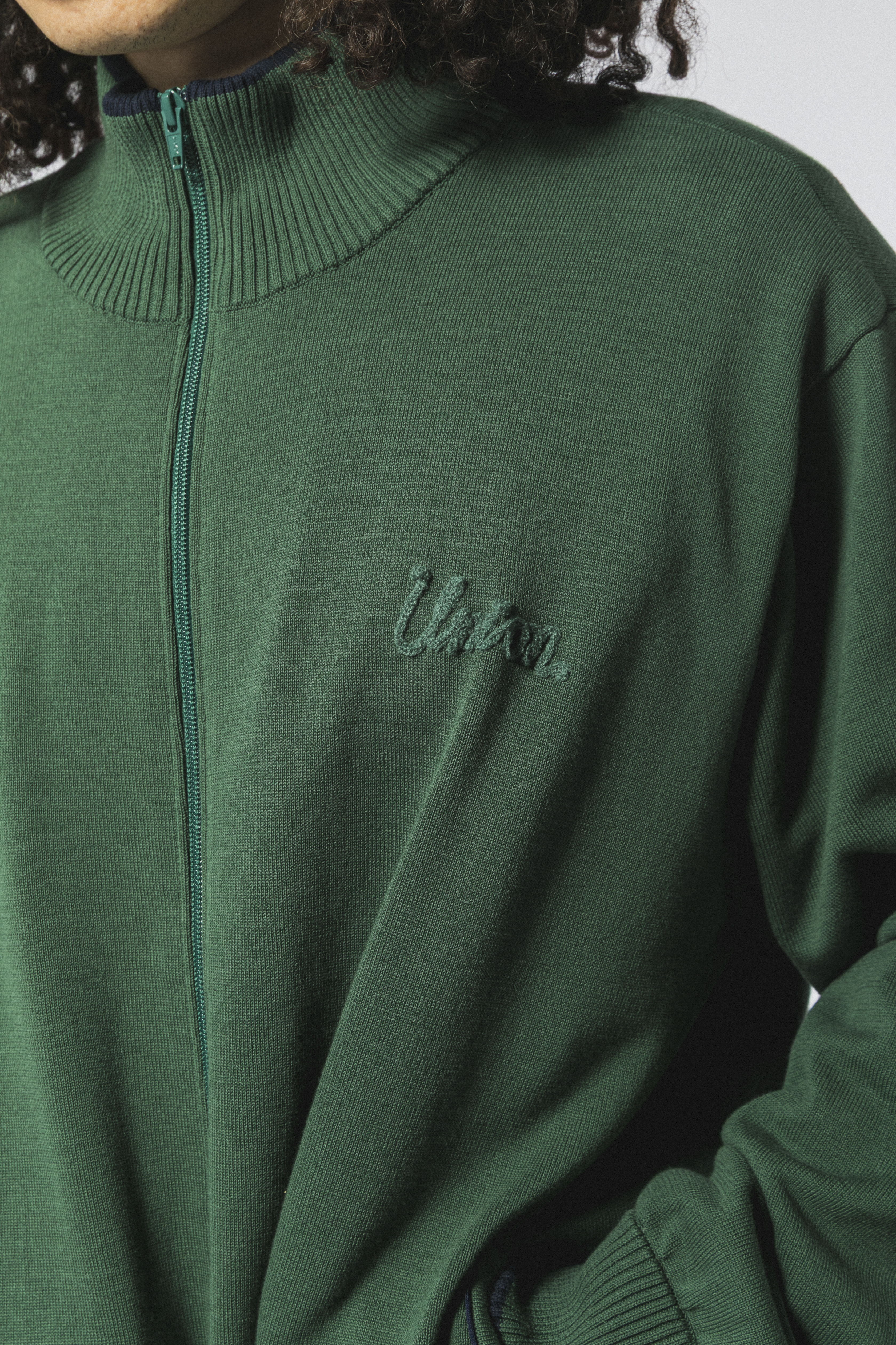 Person wearing a green zip-up sweater with embroidered text.