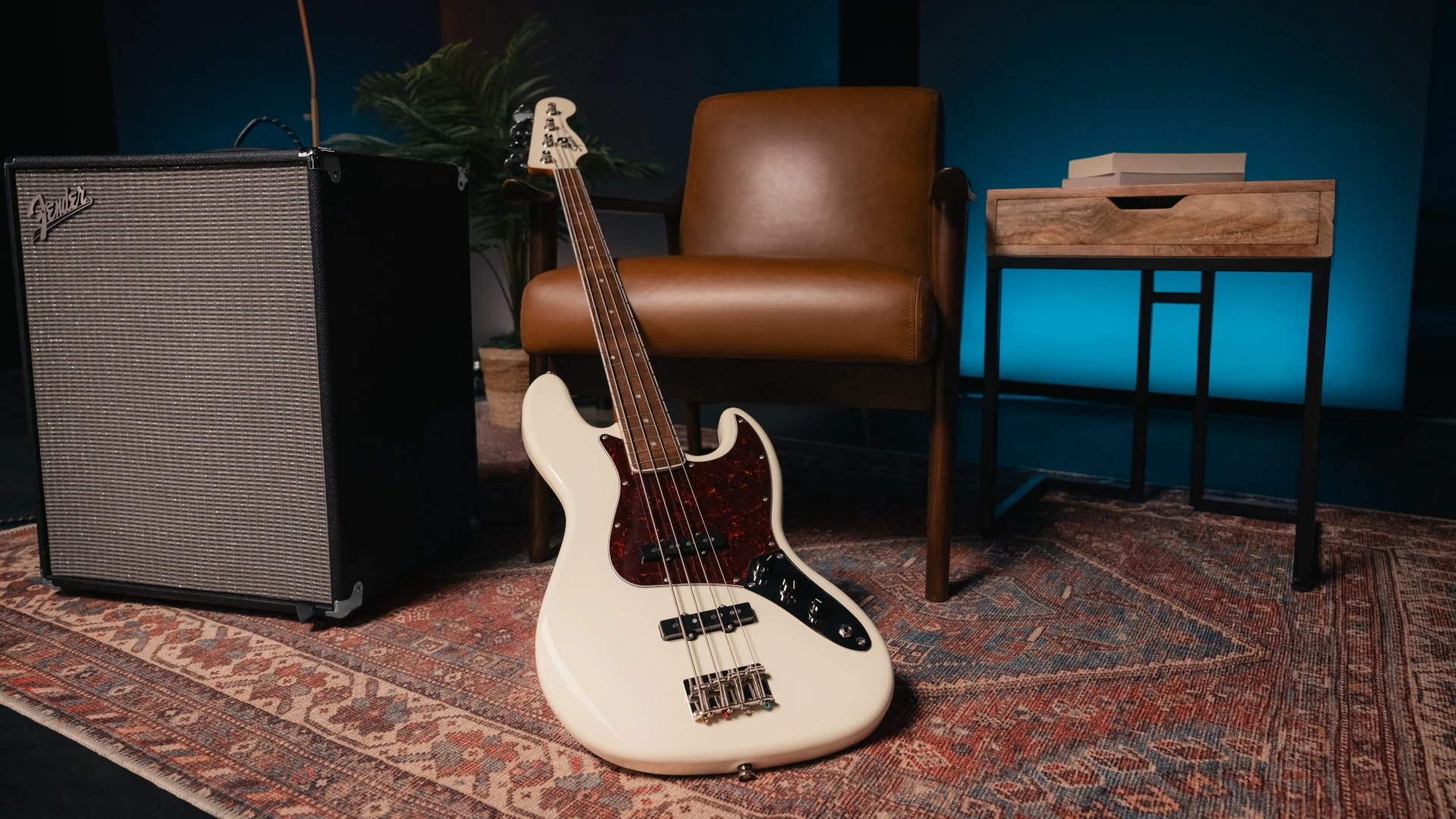A white Squier Classic Vibe Jazz Bass guitar next to a chair and amplifier on a rug.