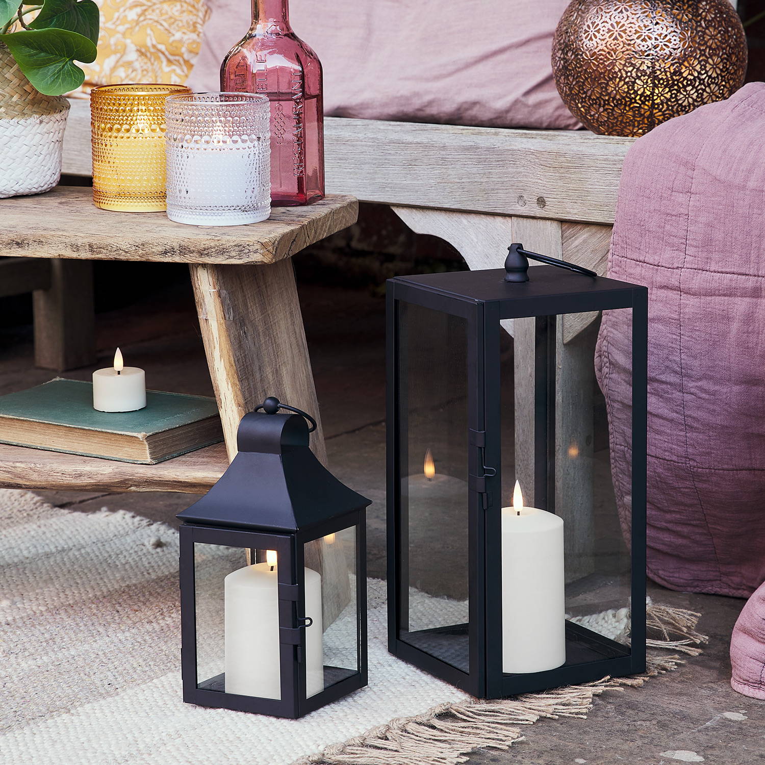 2 Black lanterns on the floor as part of an outdoor seating area.