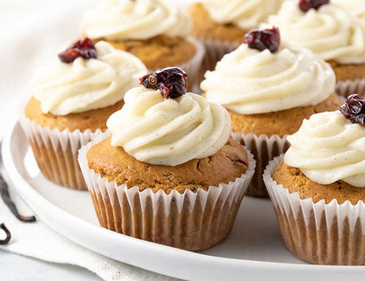 Delicious cupcakes with cream frosting and cranberry topping on a white plate.