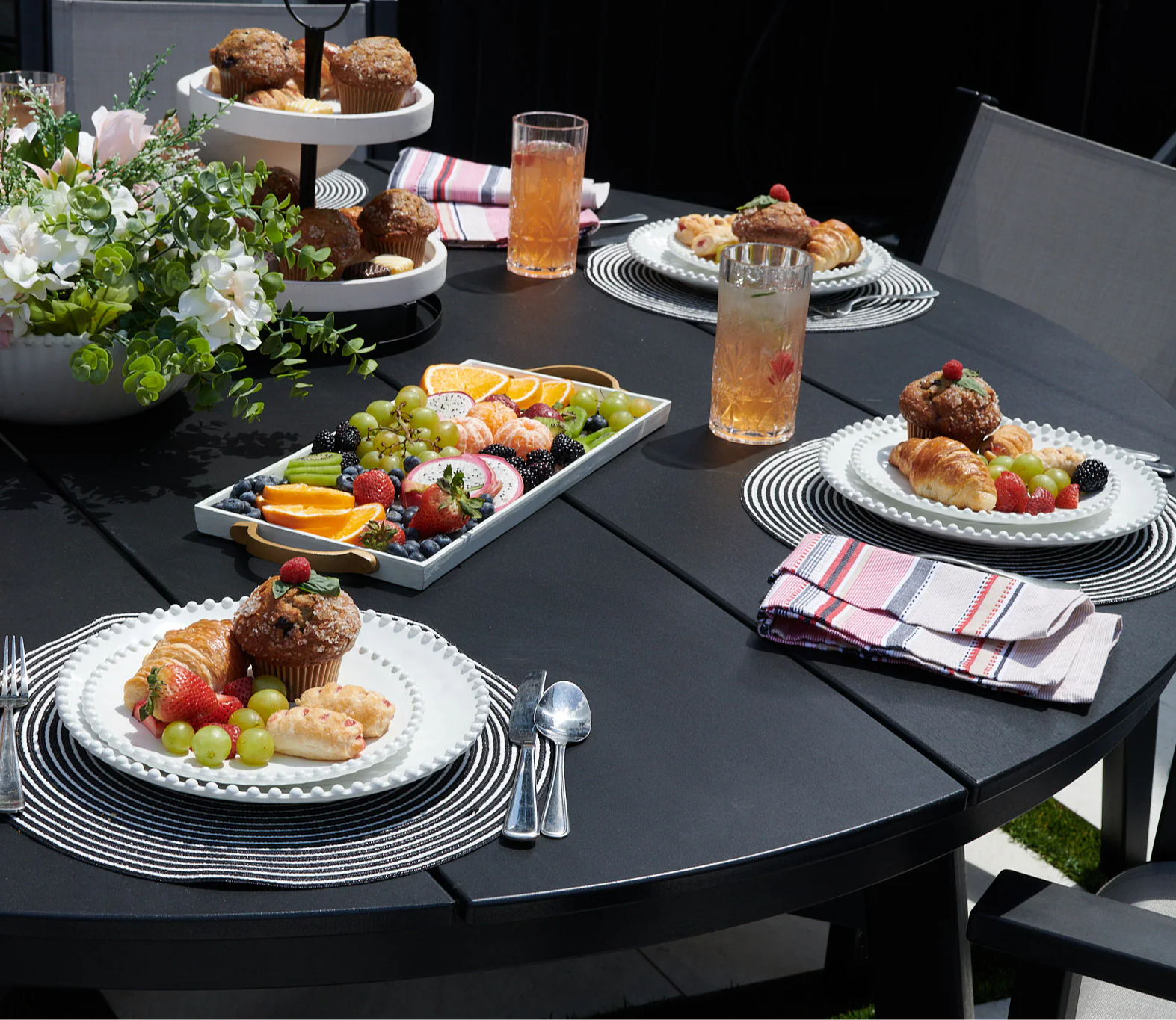 Table set with food, drinks, and floral centerpiece for outdoor dining.