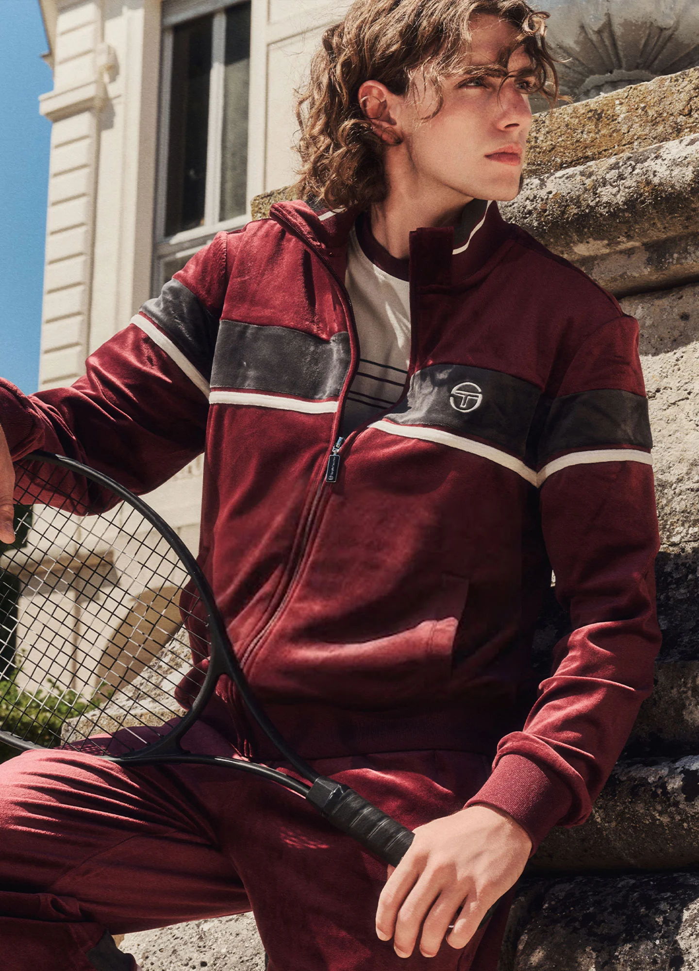 Young man in sporty Sergio Tacchini outfit holding a tennis racket outdoors.