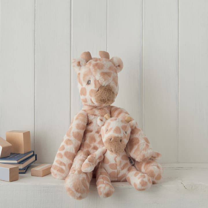 A large giraffe soft toy and a smaller version sit on a shelf with green panelling behind