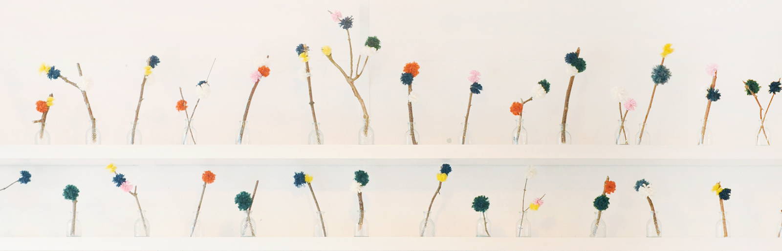 A display of home made pom poms styled on twigs in glass jars on the counterback.