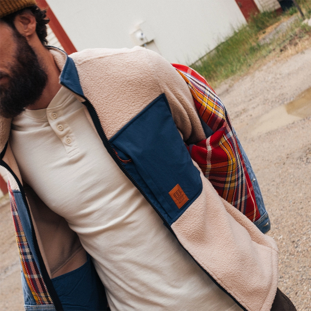 Man wearing a multi-colored jacket over a light shirt outdoors.