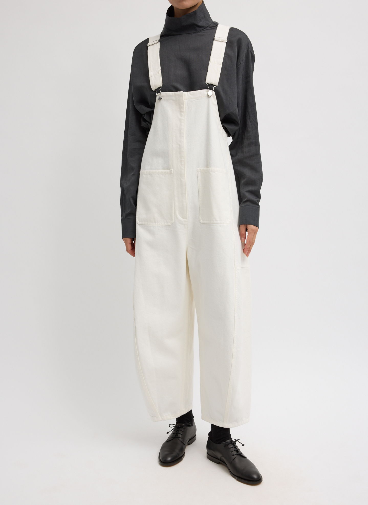 A person wearing a black turtleneck and white overalls.