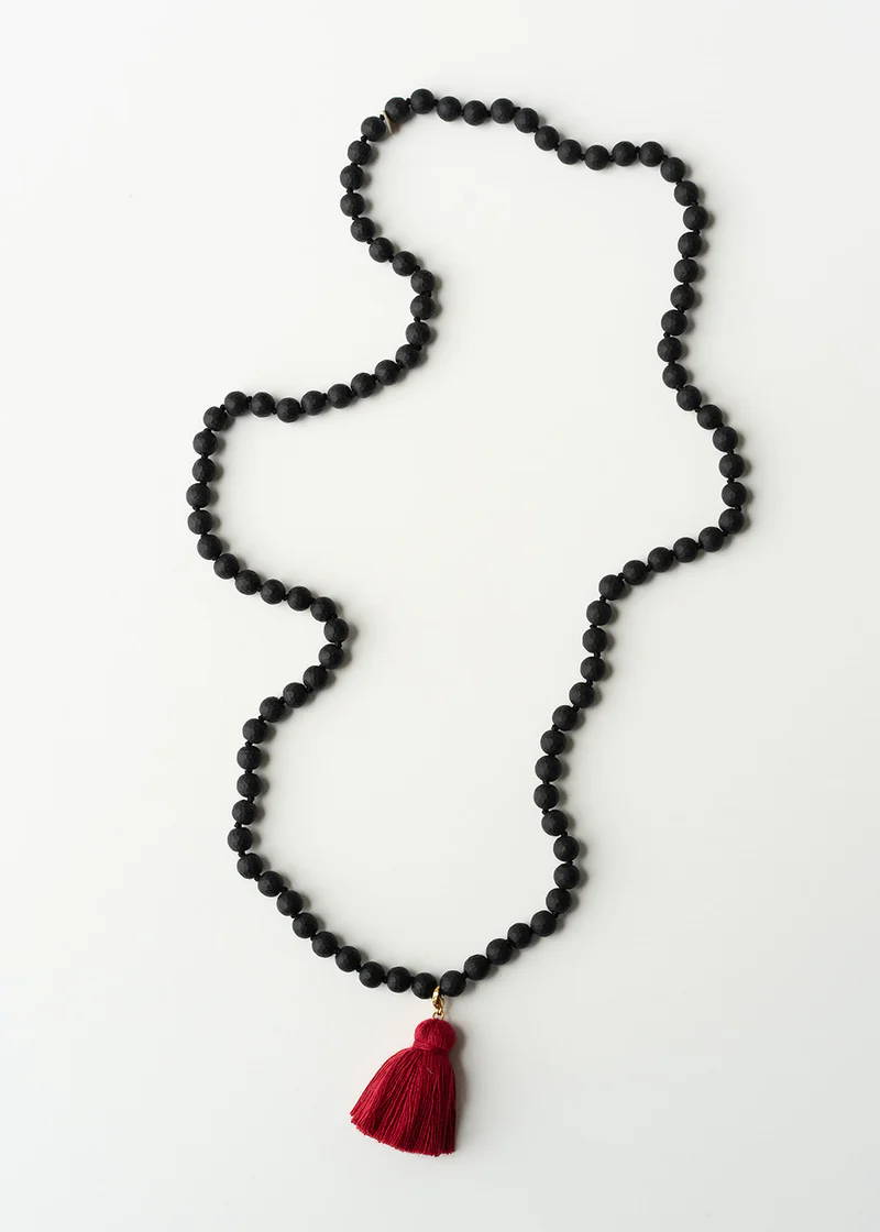 A chunky lava bead black necklace with a red tassle pendant