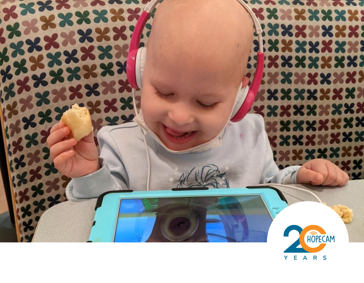 Toddler with headphones on smiling while eating a snack and watching content on an iPad