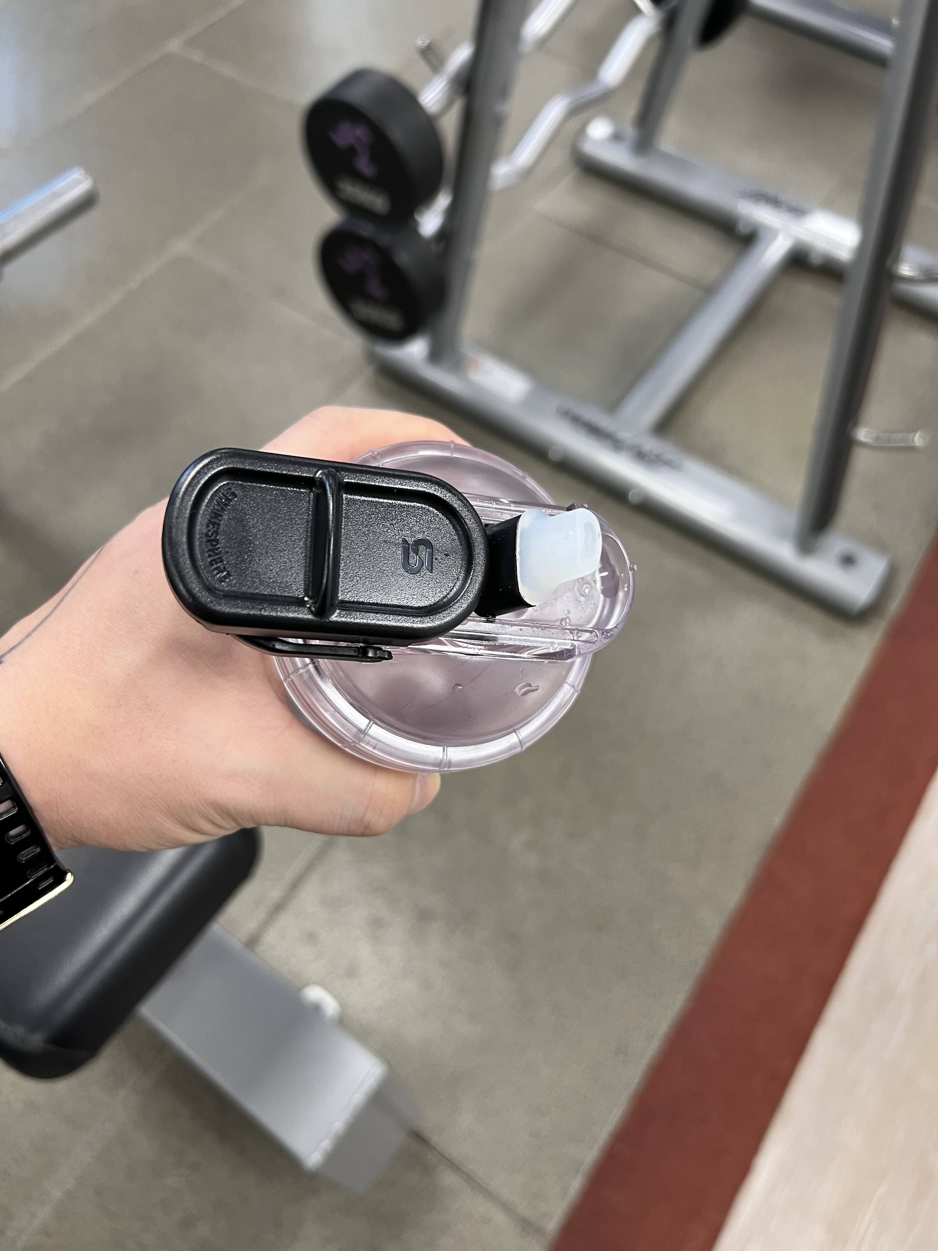 A hand holding a shaker bottle in a gym setting.
