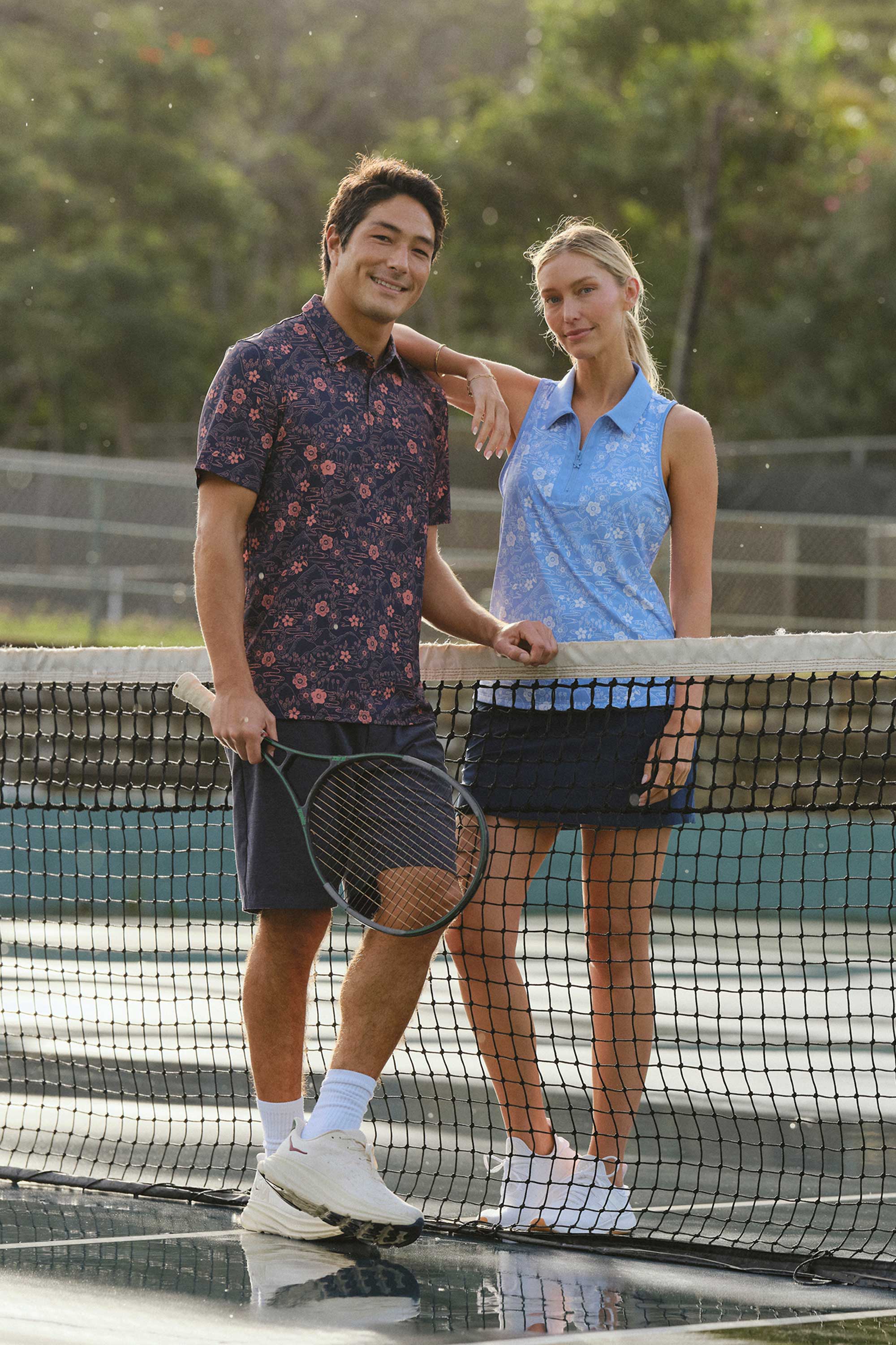 Two people posing on a tennis court with rackets.