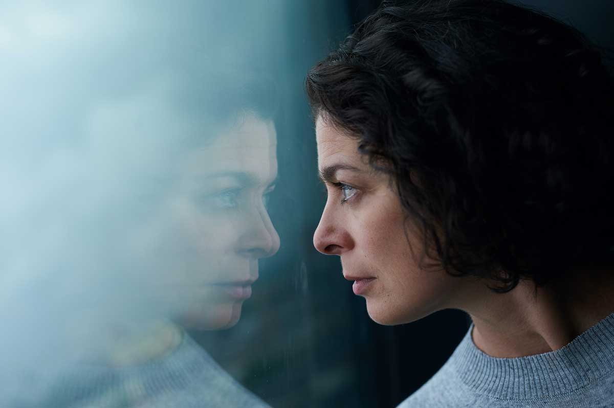 A pensive women looking out a window with her reflection showing