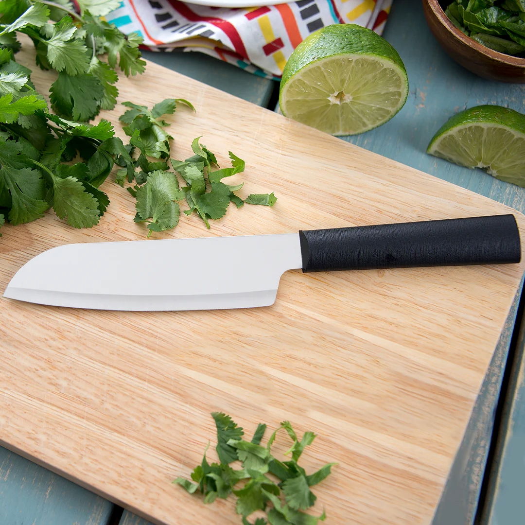 A kitchen knife on a wooden cutting board with herbs and lime.