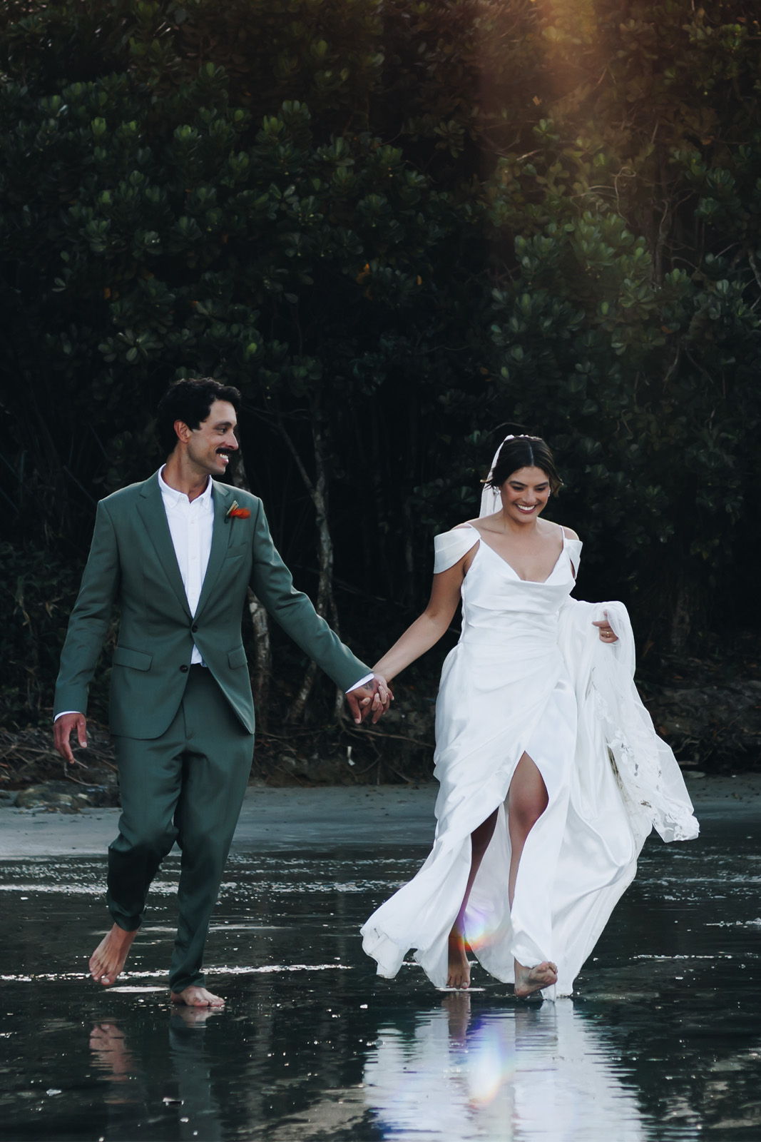 Bride and groom walking hand in hand on a beach at sunset.