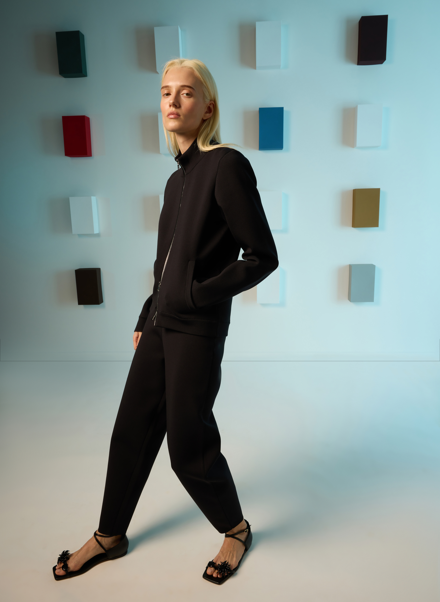 Model in black outfit poses against a colorful abstract background.