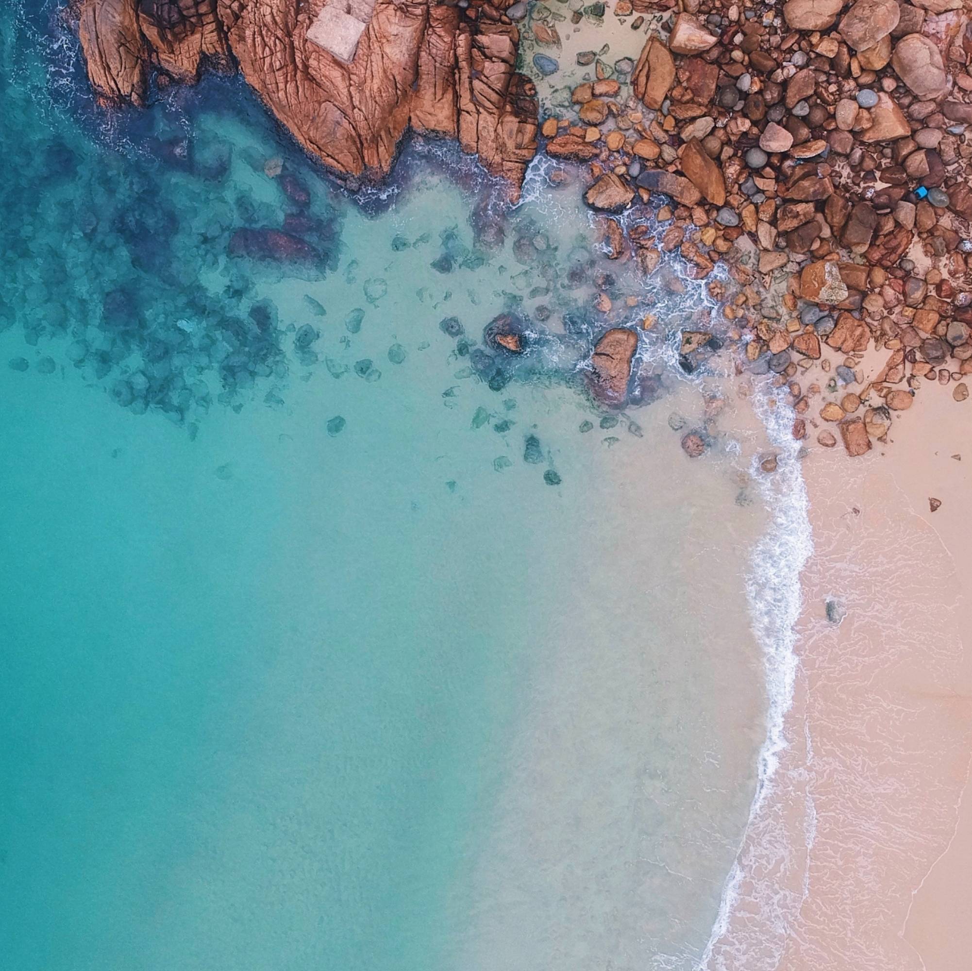 aerial shot of blue water at beach with rocks and sand CAMILLA Reducing our footprint