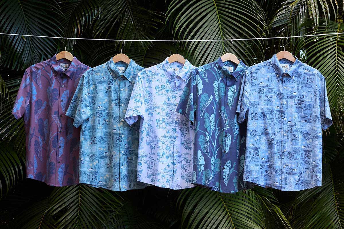 Five patterned shirts hanging against a tropical background of palm leaves.