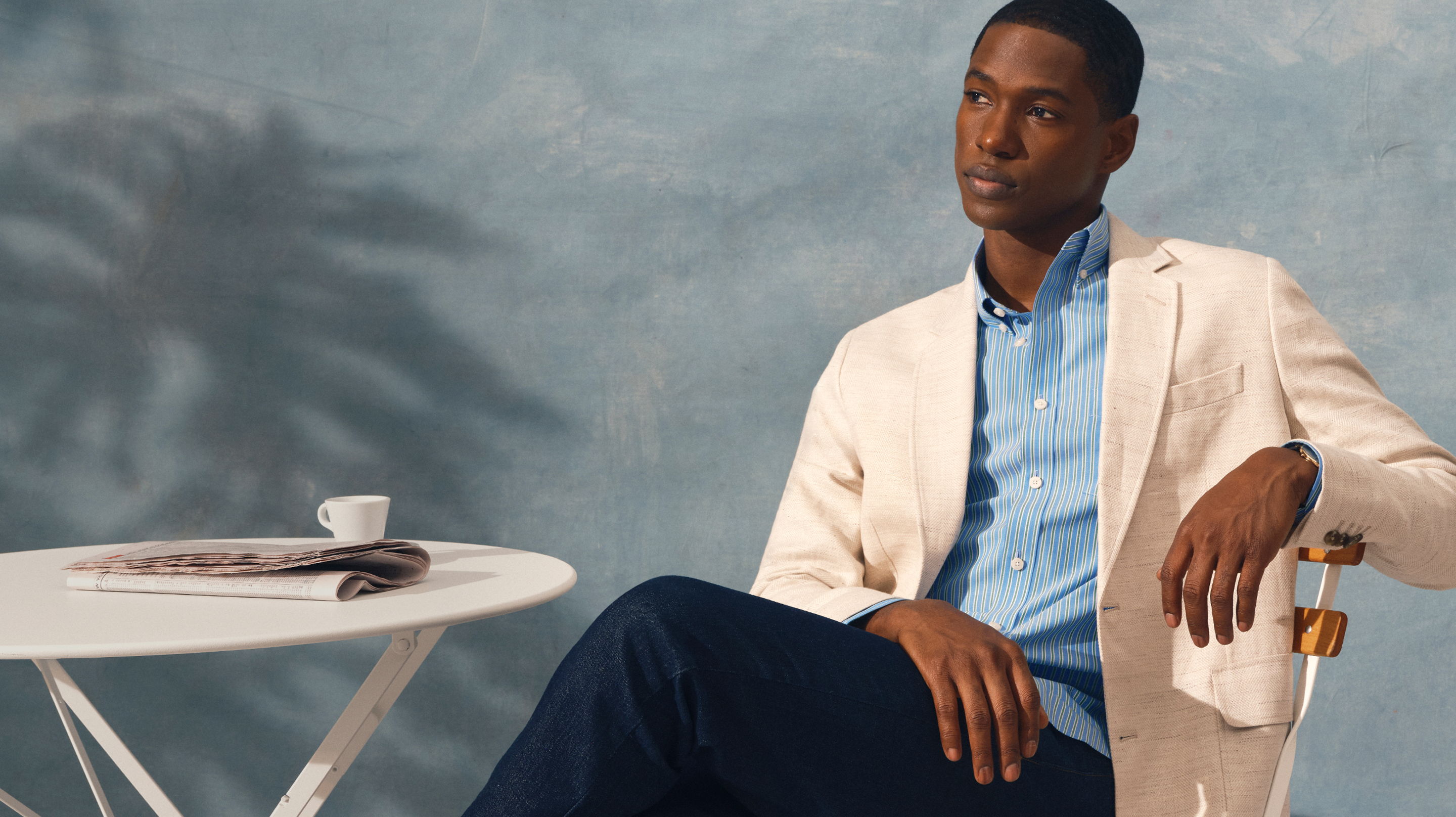 Man in a light jacket sitting by a table with a coffee cup.