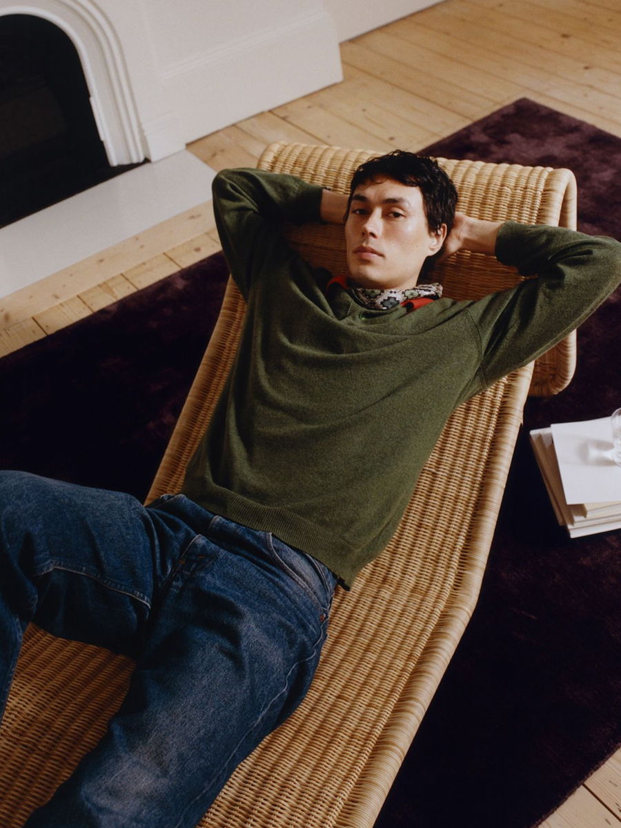 Person lying on a lounge chair, wearing a green sweater and jeans.