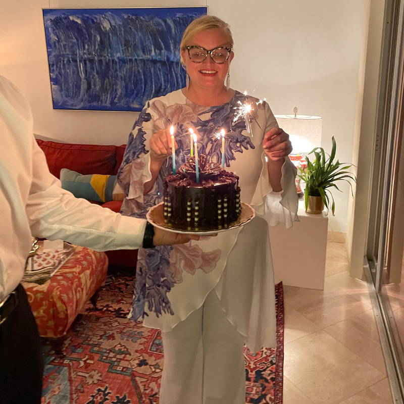 Camilla Webster wearing blue coral printed silk top with a birthday cake by Ala von Auersperg