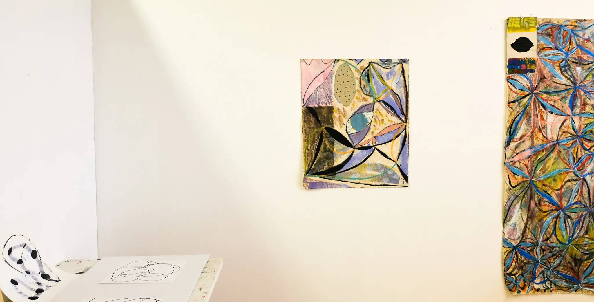 Colorful, abstract art pieces hang on the wall of the studio. 