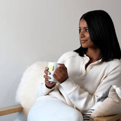 Person sitting with a mug, wearing a cozy white outfit.