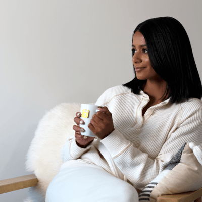 Person sitting with a mug, wearing a cozy white outfit.