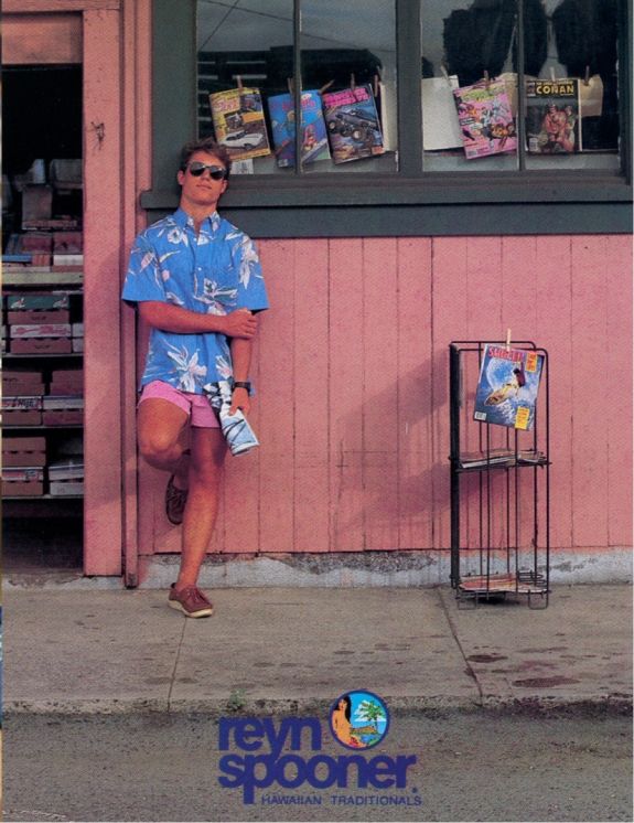 Person in a blue shirt leaning against a pink wall. Magazines displayed nearby.