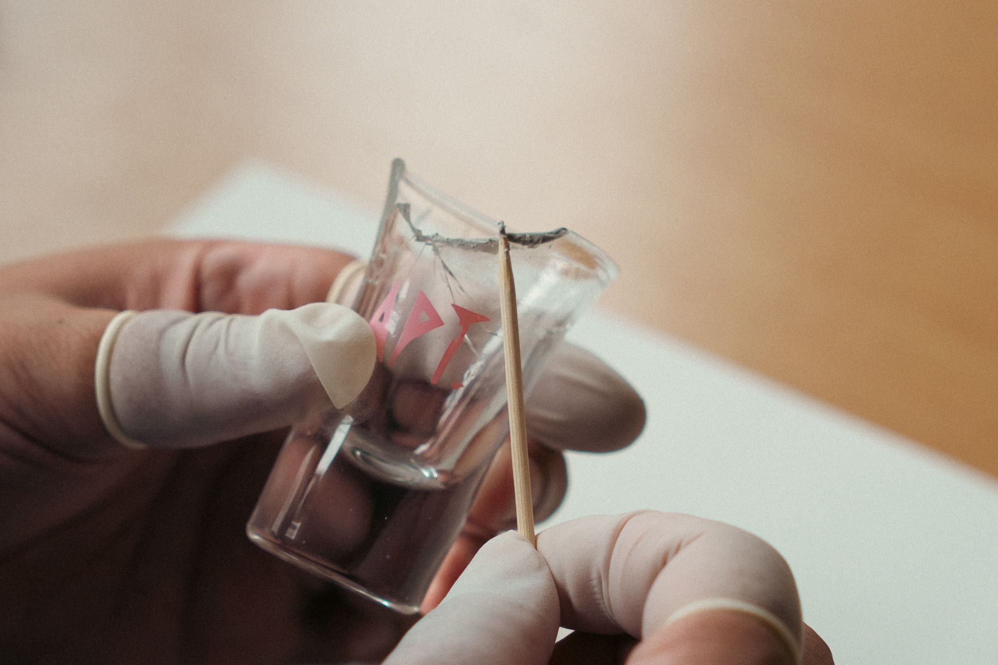 A gloved hand holding a small glass container with a stick.