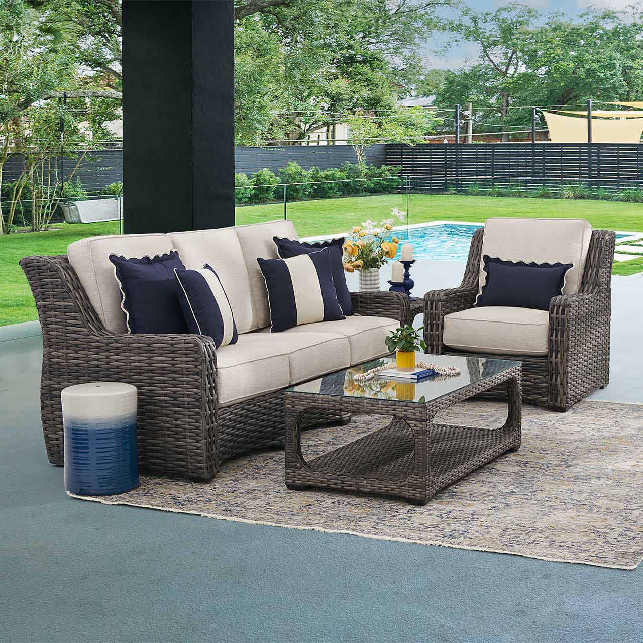 Outdoor seating arrangement with cushions, coffee table, and a pool view.