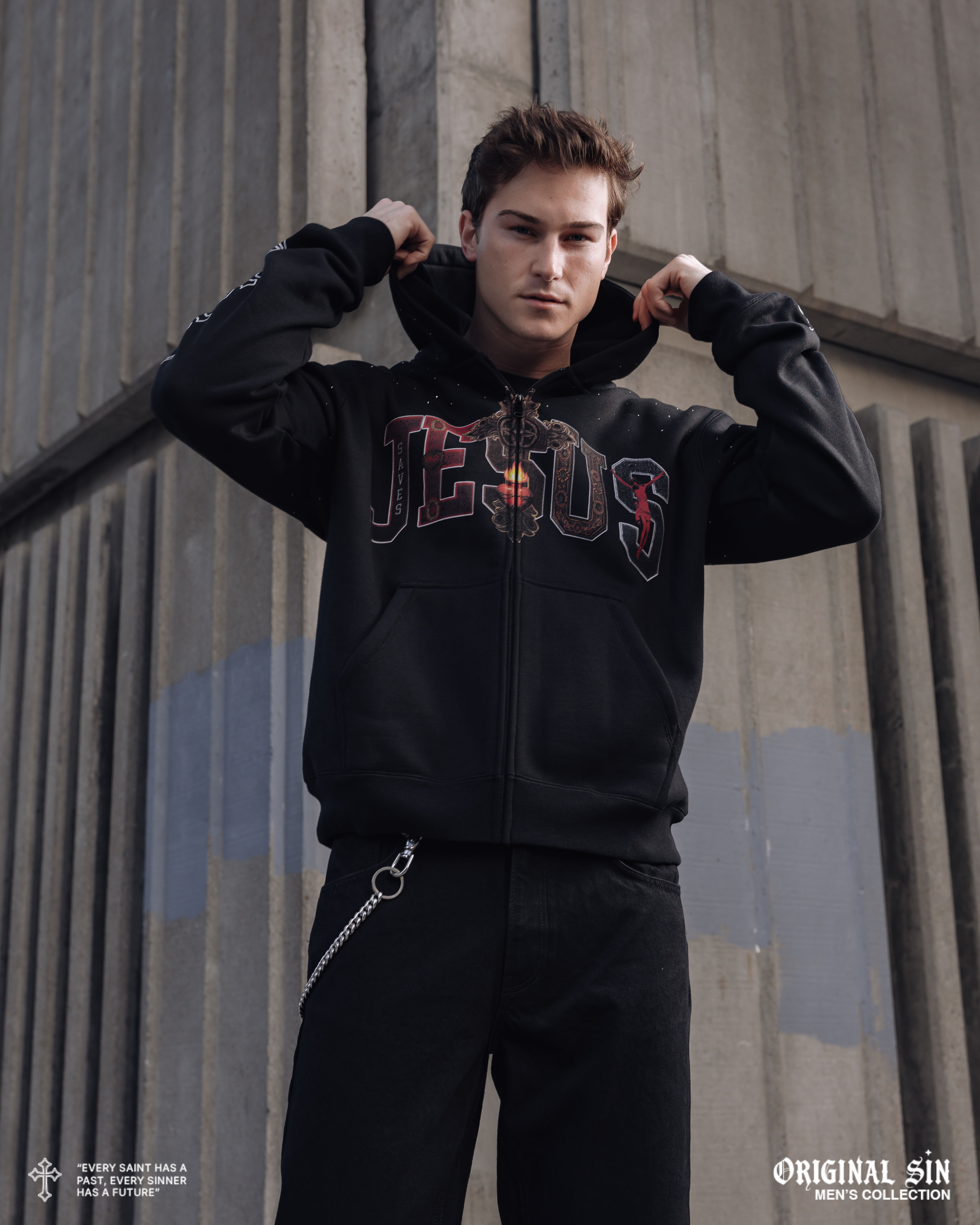 Young man in a black hoodie posing against a concrete background.
