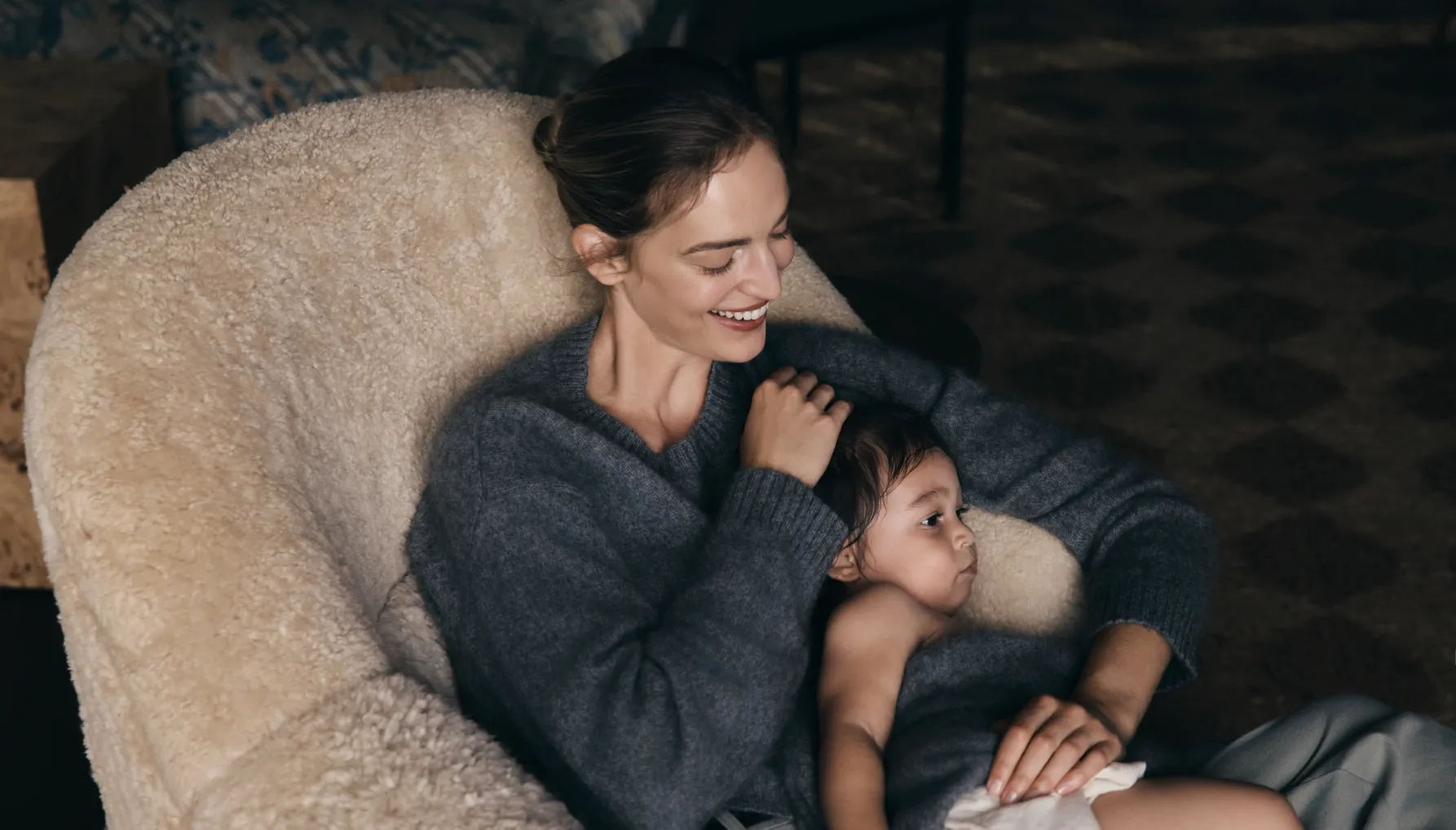 A woman cuddles a child in a cozy chair.