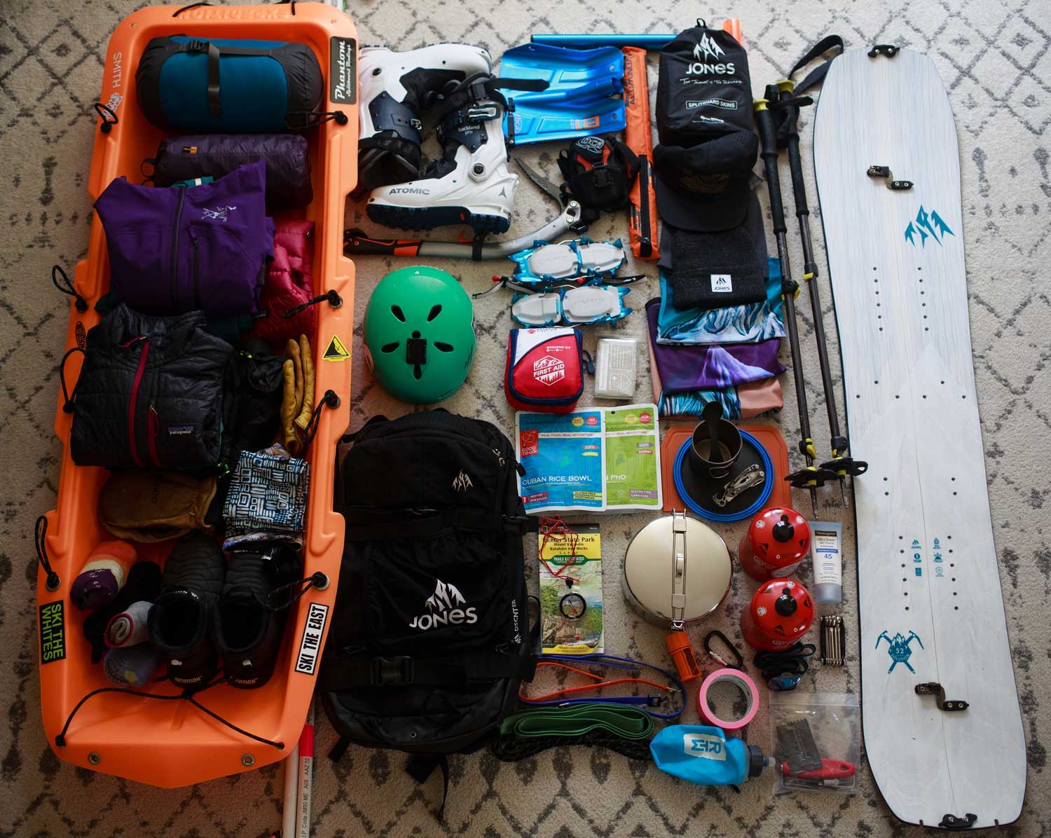 Assorted outdoor gear arranged on a surface, including a splitboard, and safety equipment.