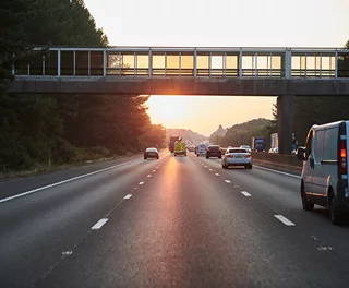 Sunset over a highway with a pedestrian bridge in the background.