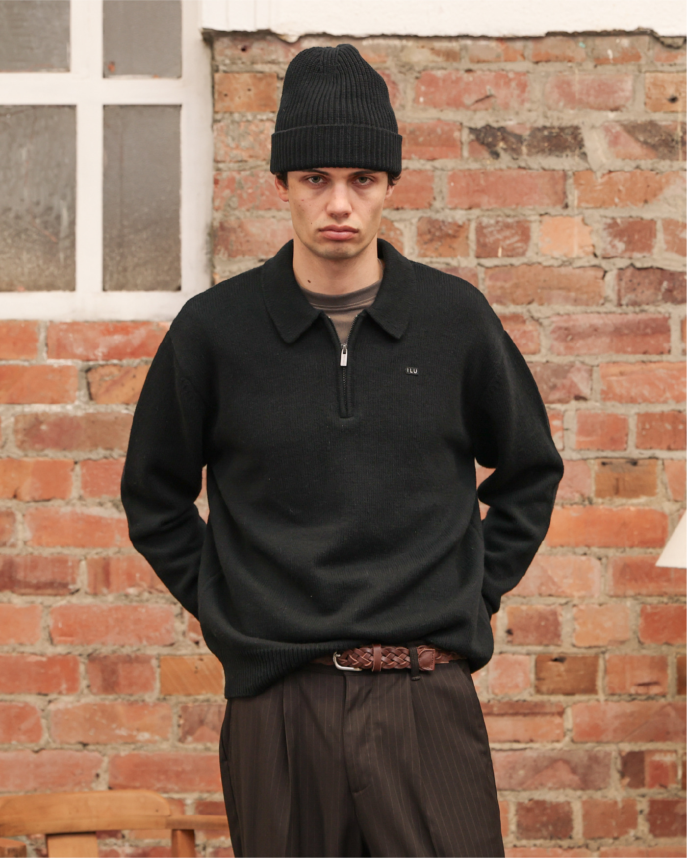 Person wearing a black sweater and beanie, standing against a brick wall.